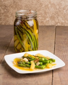 Photo of a white plate with pickled asparagus on it, a jar of pickled asparagus in the background