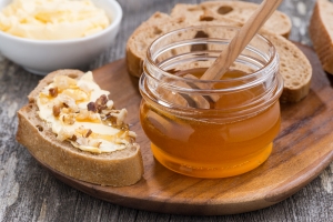 Photo of a jar of honey next to bread with butter, honey, and nuts on top