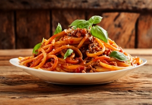 Photo of a plate loaded with spaghetti noodles and sauce garnished with basil leaves