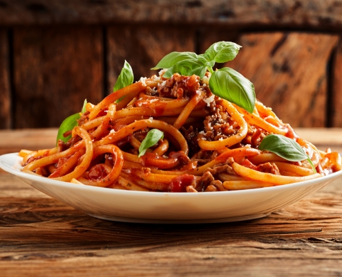Photo of a plate loaded with spaghetti noodles and sauce garnished with basil leaves